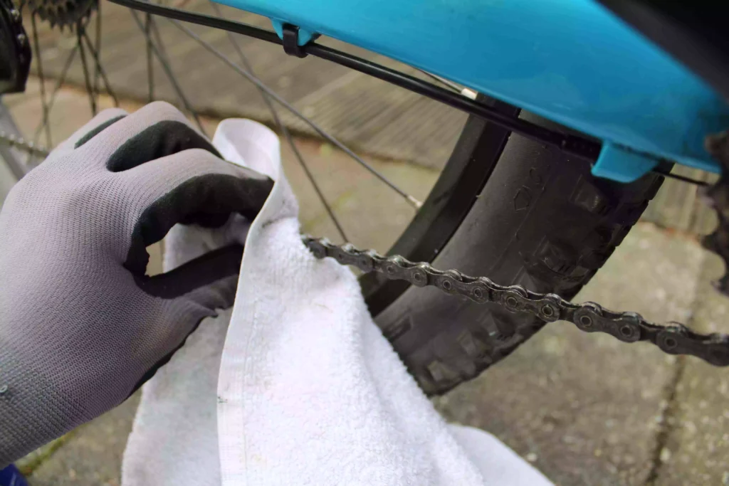 Met witte handdoek en handschoen een ketting schoonmaken van een MTB